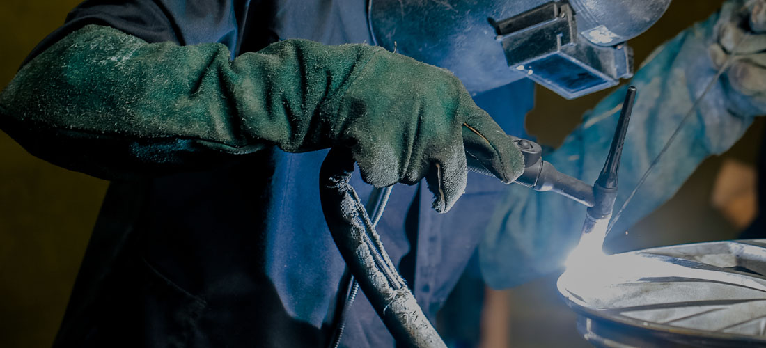 A wheel collision technician using a welding machine to refurbish an alloy wheel